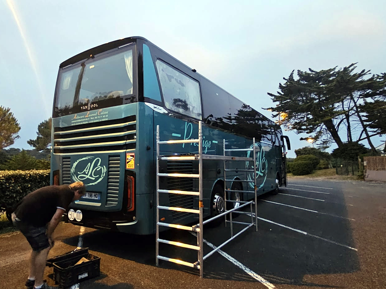 A Van Hool coach beside a mobile work platform, with a technician and tools nearby.