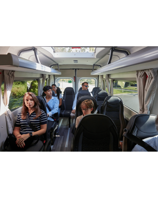 Passengers inside an IVECO eFLEXY minibus, with large side windows and overhead glazing bringing light into the cabin.